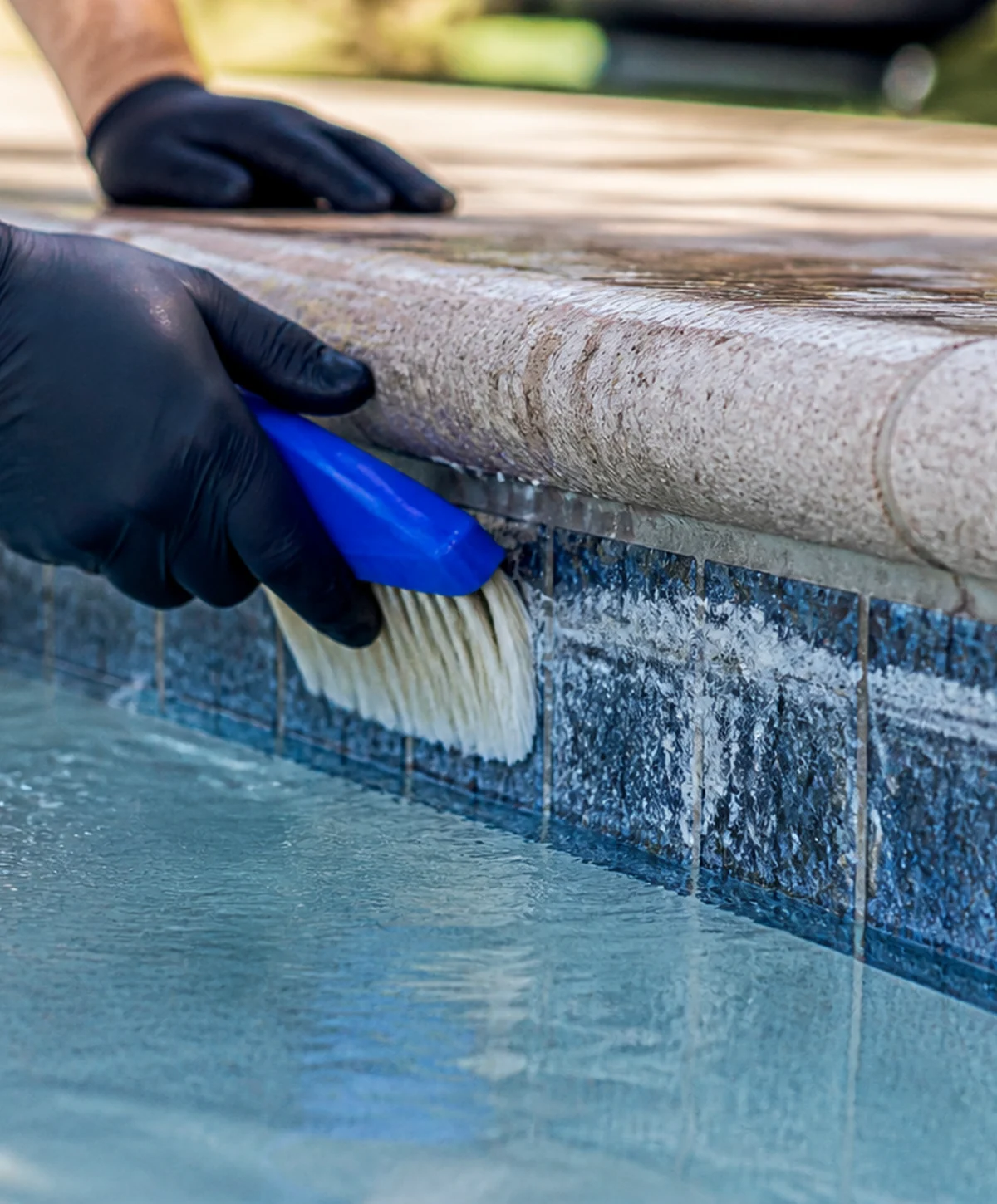 Close-up of visible mineral buildup along a residential and commercial pool tile line being professionally evaluated for cleaning.